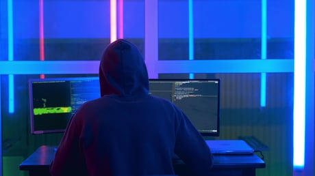 hacker in hoodie working two monitors